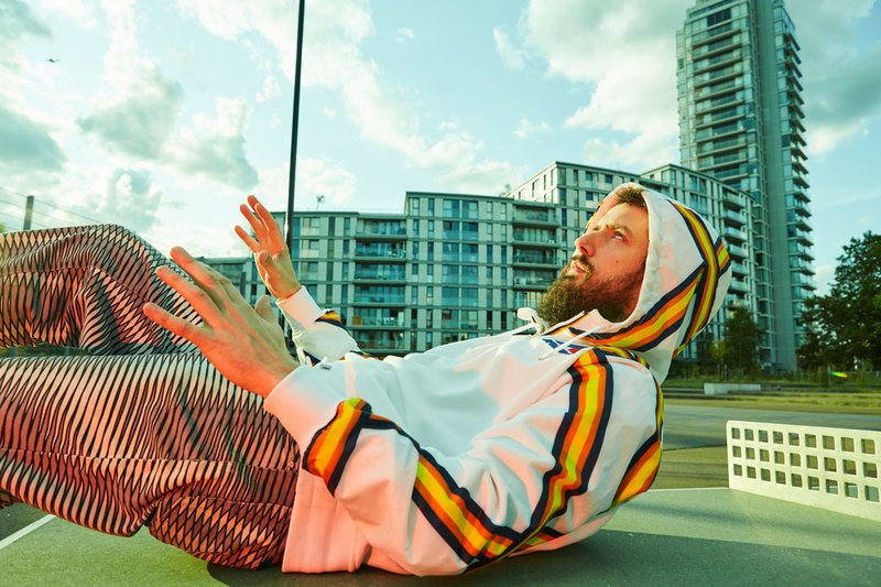 A hooded Danalogue (aka Dan Leavers) reclining on an outdoor table tennis table with a block of flats in the background